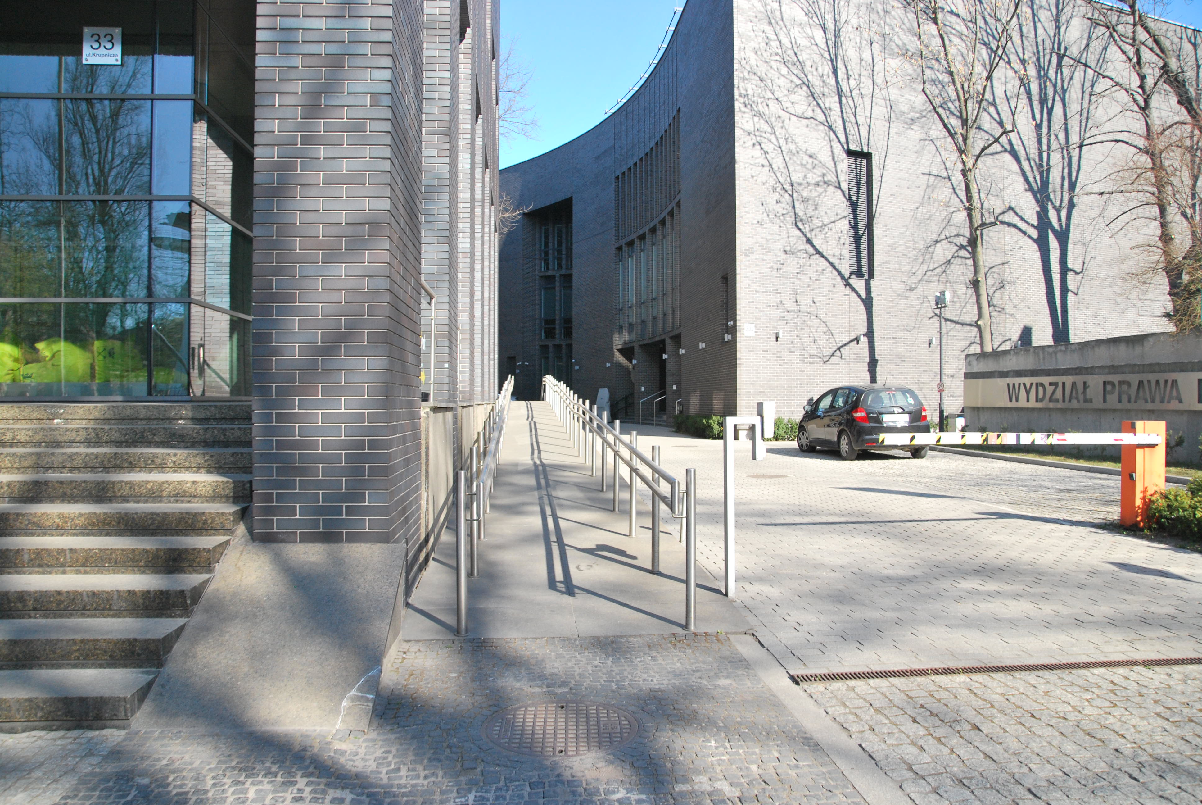 Na środku znajduje się podjazd dla osób poruszających się na wózkach. Po lewej stronie widoczne są schody prowadzące do Auditorium Maximum. Po lewej znajduje się budynek Wydziału Prawa i Administracji UJ, wjazd na wewnętrzny parking możliwy jest po minięciu znajdującej się na pierwszym planie rampy.